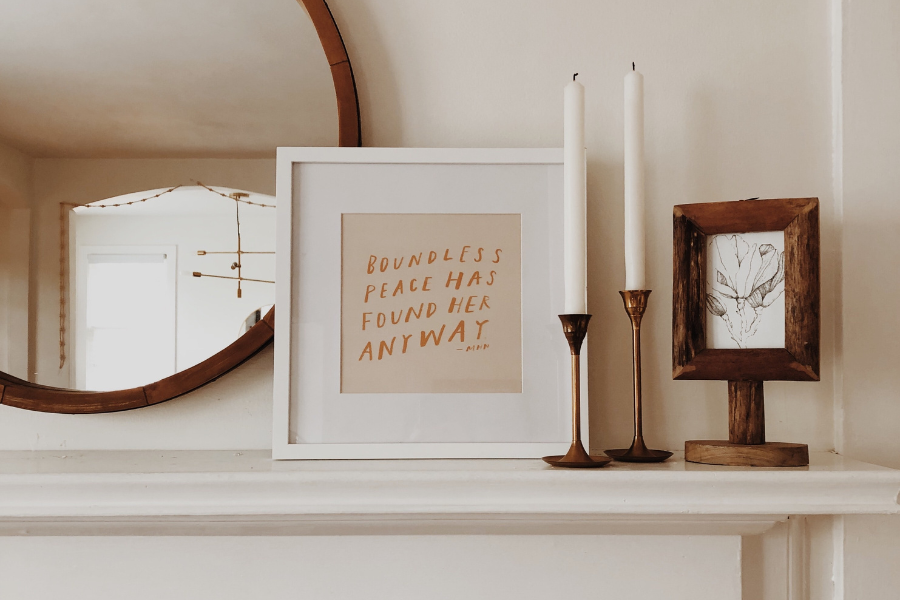 Framed art and candles sitting on a fireplace mantel.