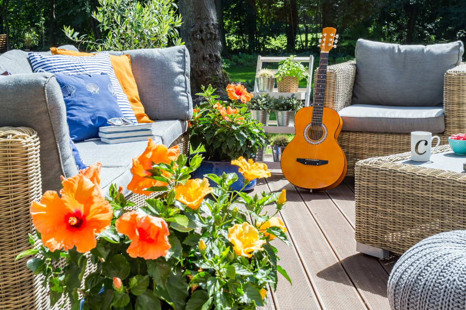 Wicker patio set with sky blue cushions and bright orange accent cushions. A guitar rests against one of the chairs and orange flowers take up the bottom left of the frame