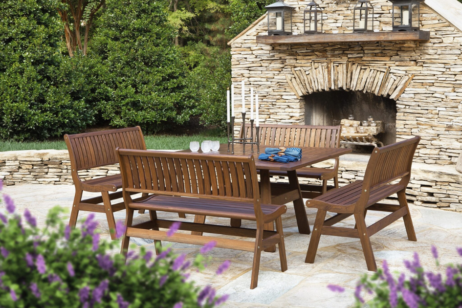 A wood patio set nestled amongst greenery and flowers with a stone fireplace just behind