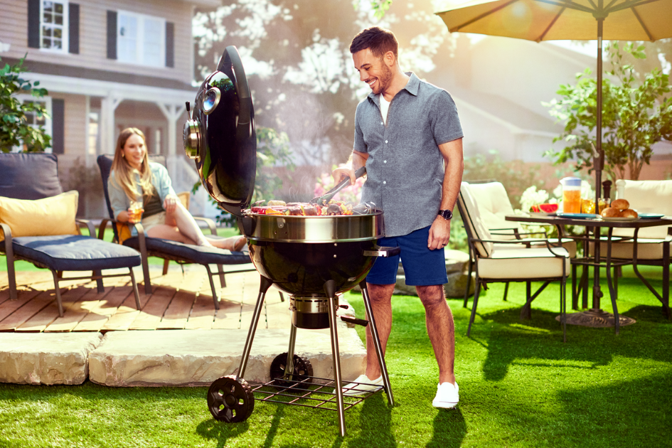 A man grilling on his charcoal BBQ in his backyard.